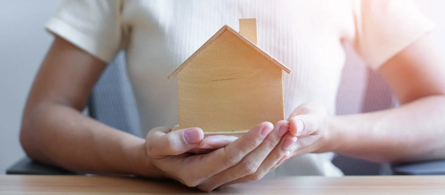 Person holding a small wooden house model in both hands